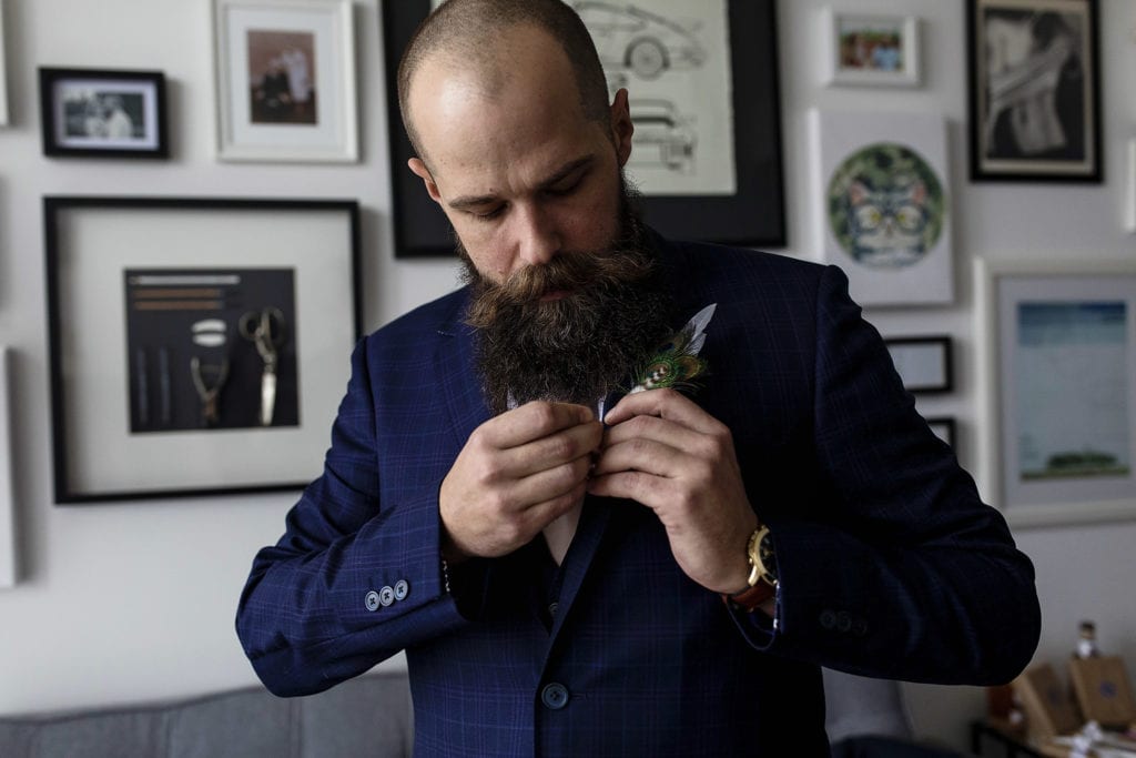 groom in blue suit fastens peacock feather boutonniere