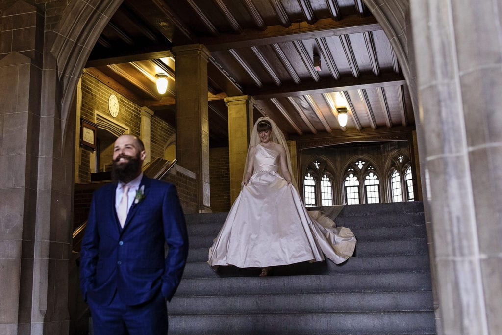 bride walks down staircase towards waiting groom during first look for Hart House Toronto wedding