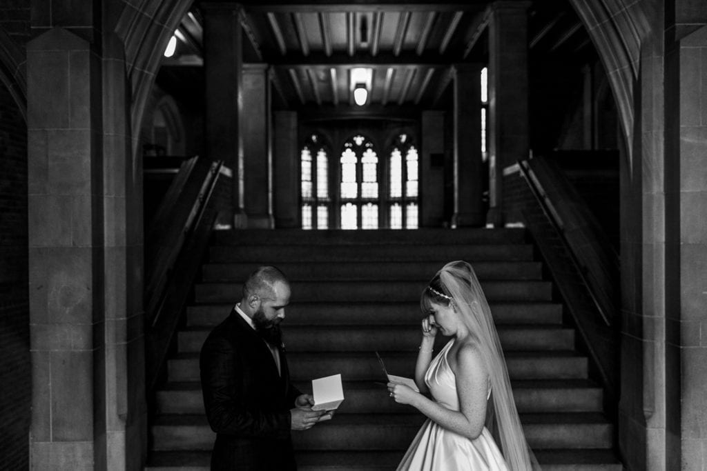 bride wipes tear as she stands with groom while each reads note