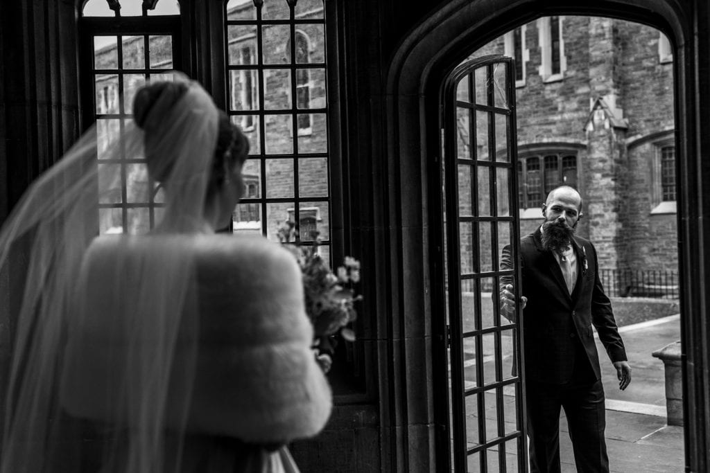groom holds door and looks at bride as she walks towards him