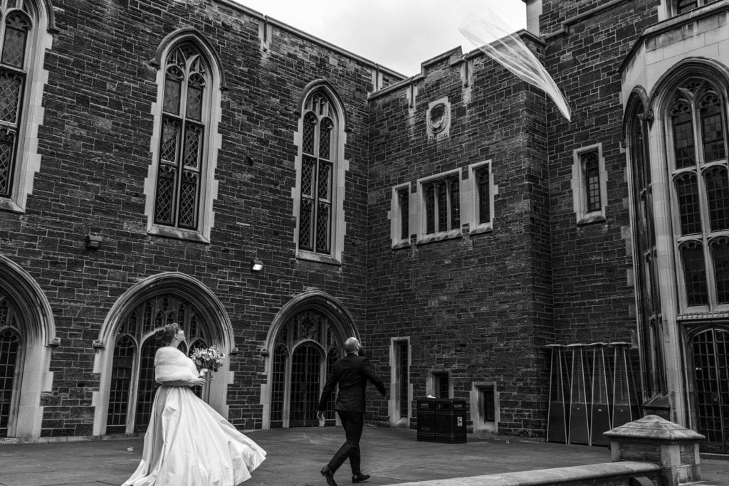bride looks up at veil as it blows away and groom walks towards it to catch it