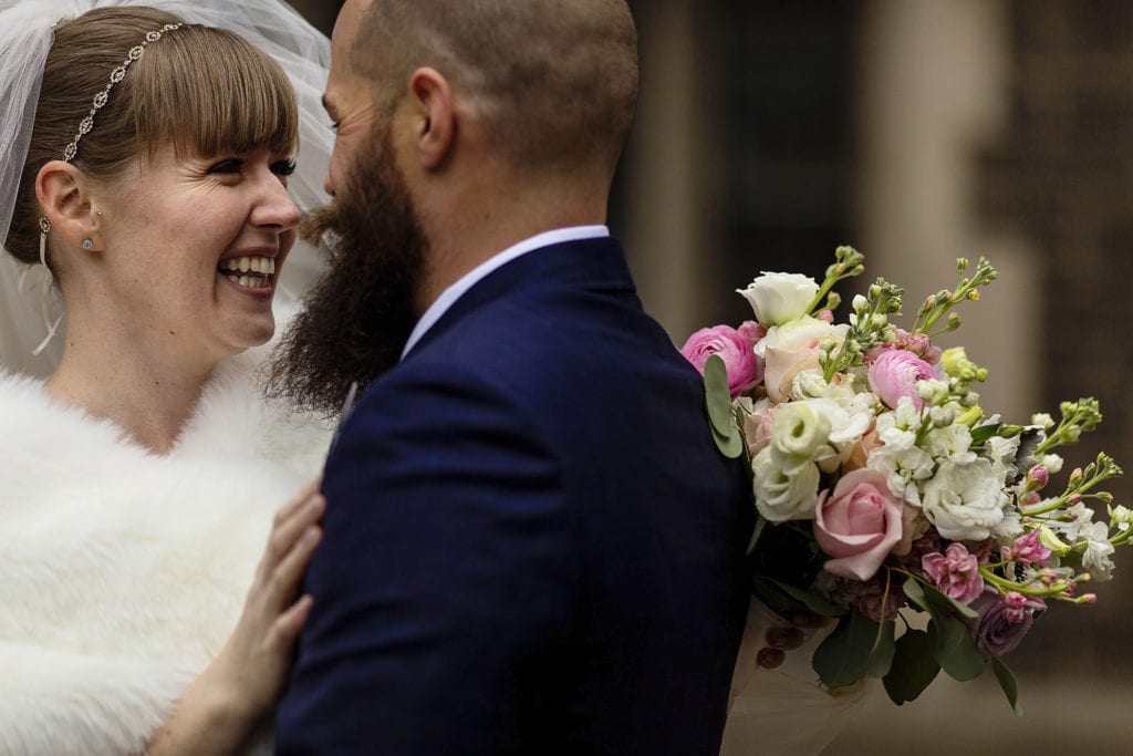 bride looks at groom while laughing and holding flowers behind him