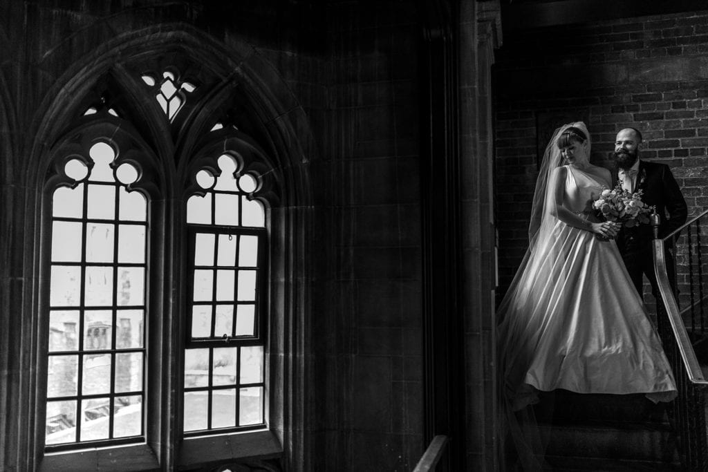 bride and groom stand on stairs in window light with old fashioned window in foreground