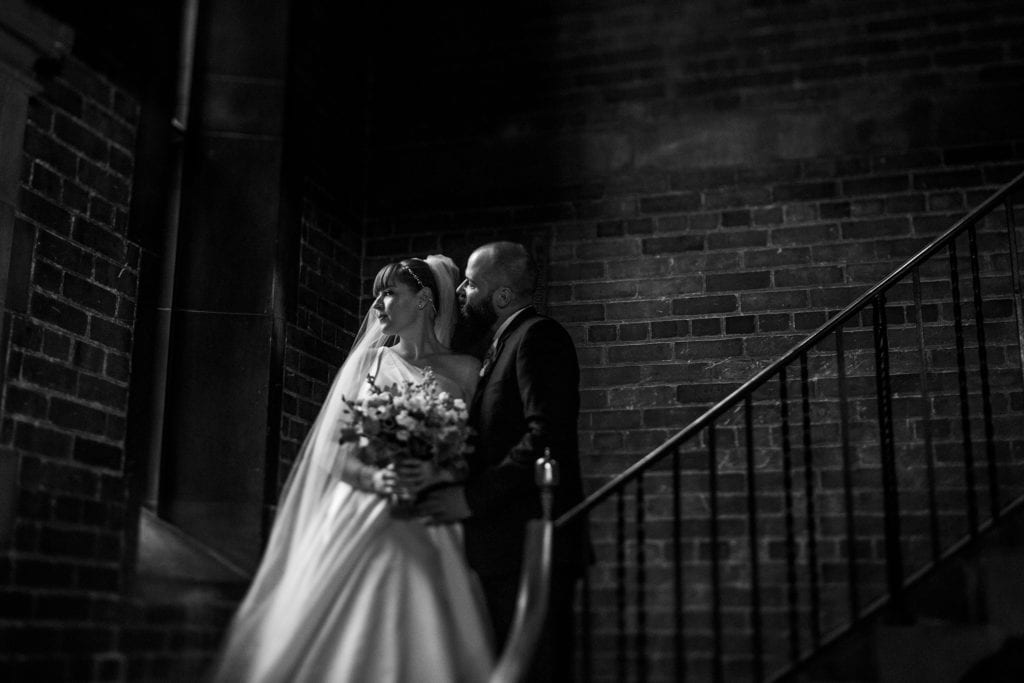 bride looks out window while groom stands on stairs beside her