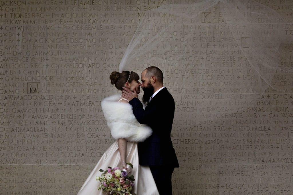 groom holds bride's face close to his while veil blows high behind them