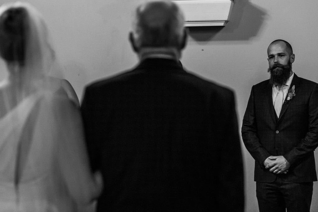 groom looks at bride as she approaches with father