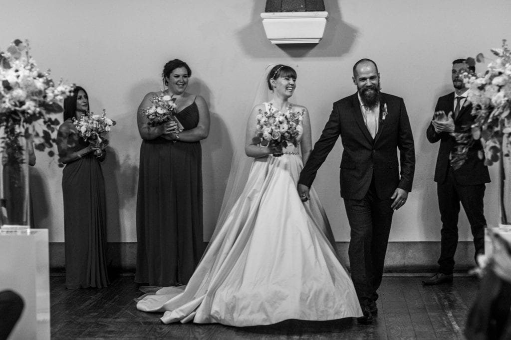 bride and groom smile and hold hands while preparing to leave wedding ceremony