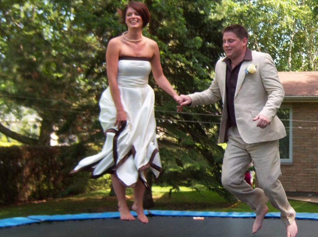 couple in wedding attire jumping on trampoline
