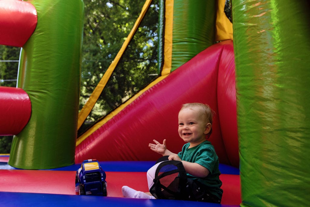 toddler raises hands in shrug inside red bouncy house