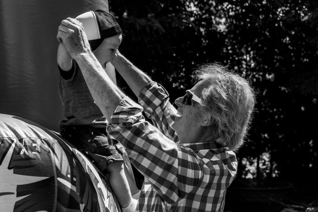 smiling grandfather holds toddler's arms up