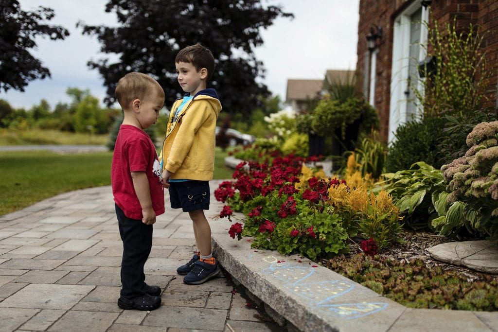boy in red shirt stands beside boy in yellow sweater facing opposite directions