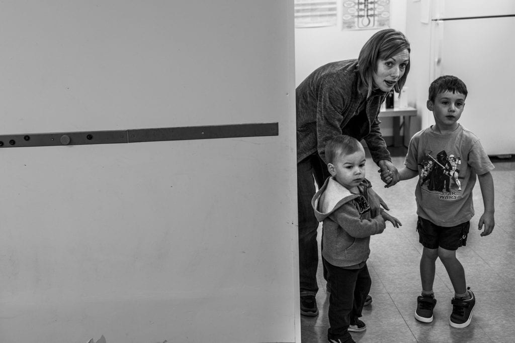 woman hunches next to two small boys, looking into distance inside building