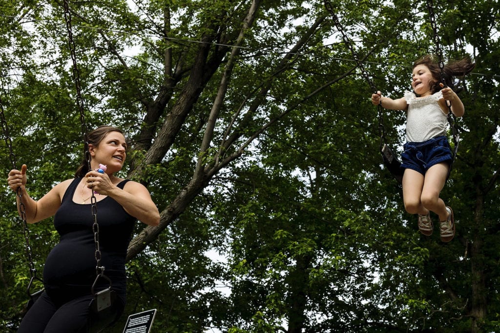 pregnant mom on swing looks up at daughter swinging high