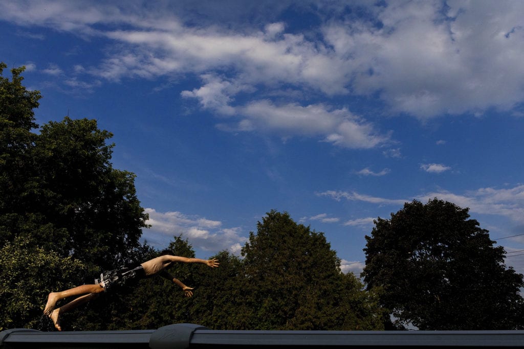 boy in swim trunks dives into pool with blue sky in the background