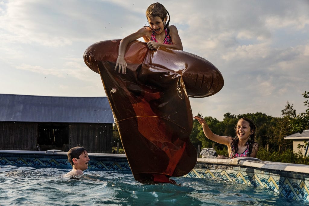 girl holding poop emoji pool toy flies in air into pool in front of brother and sister