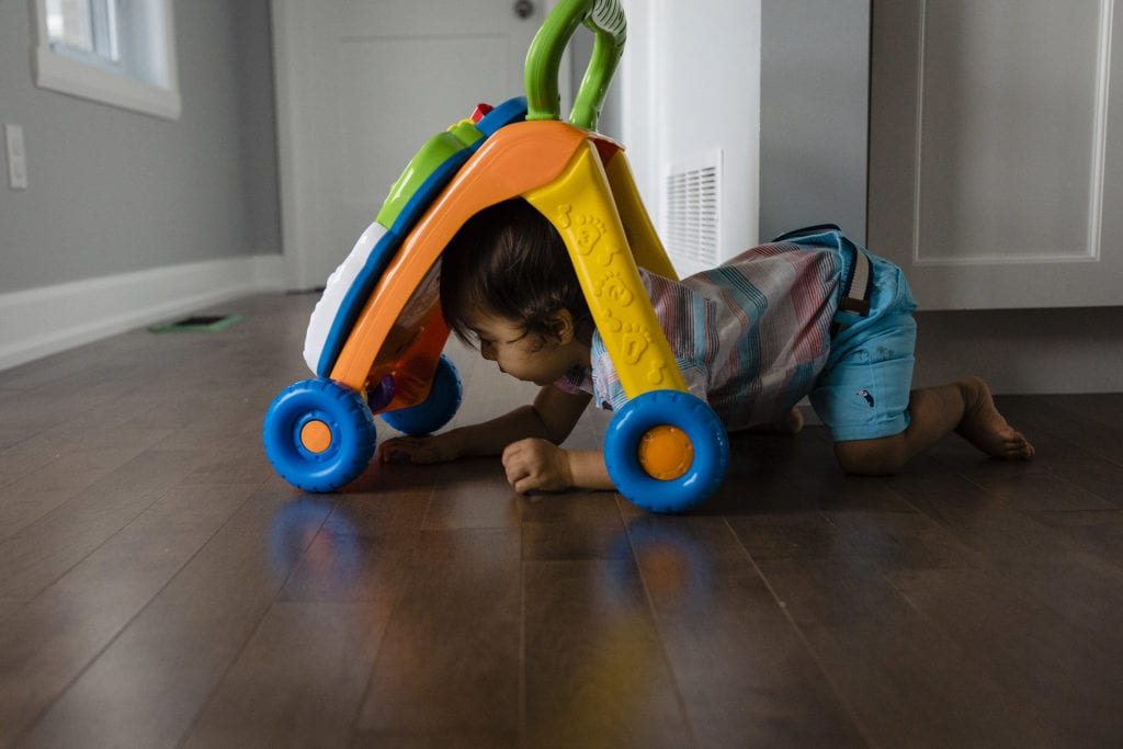 toddler crawls on floor under small plastic toy