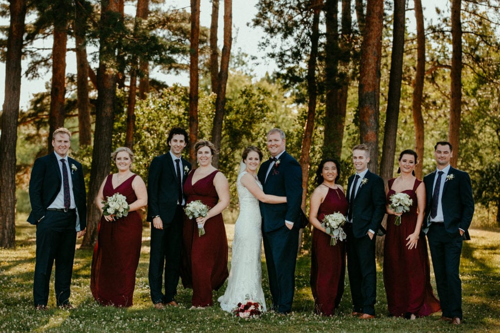 wedding party in charcoal and burgundy stand amongst pine trees