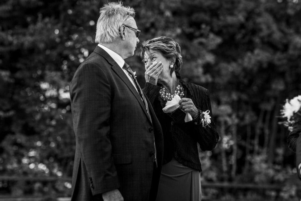 man looks at woman in mother of the groom dress as she holds her hand over her mouth