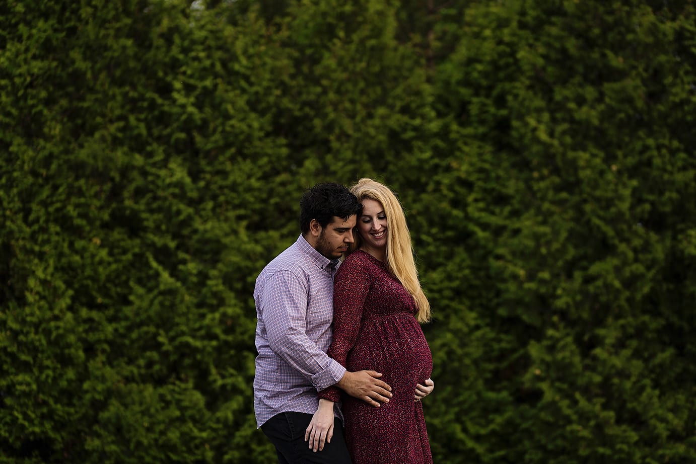 pregnant woman cuddles with husband in front of hedge for Cornwall countryside maternity session