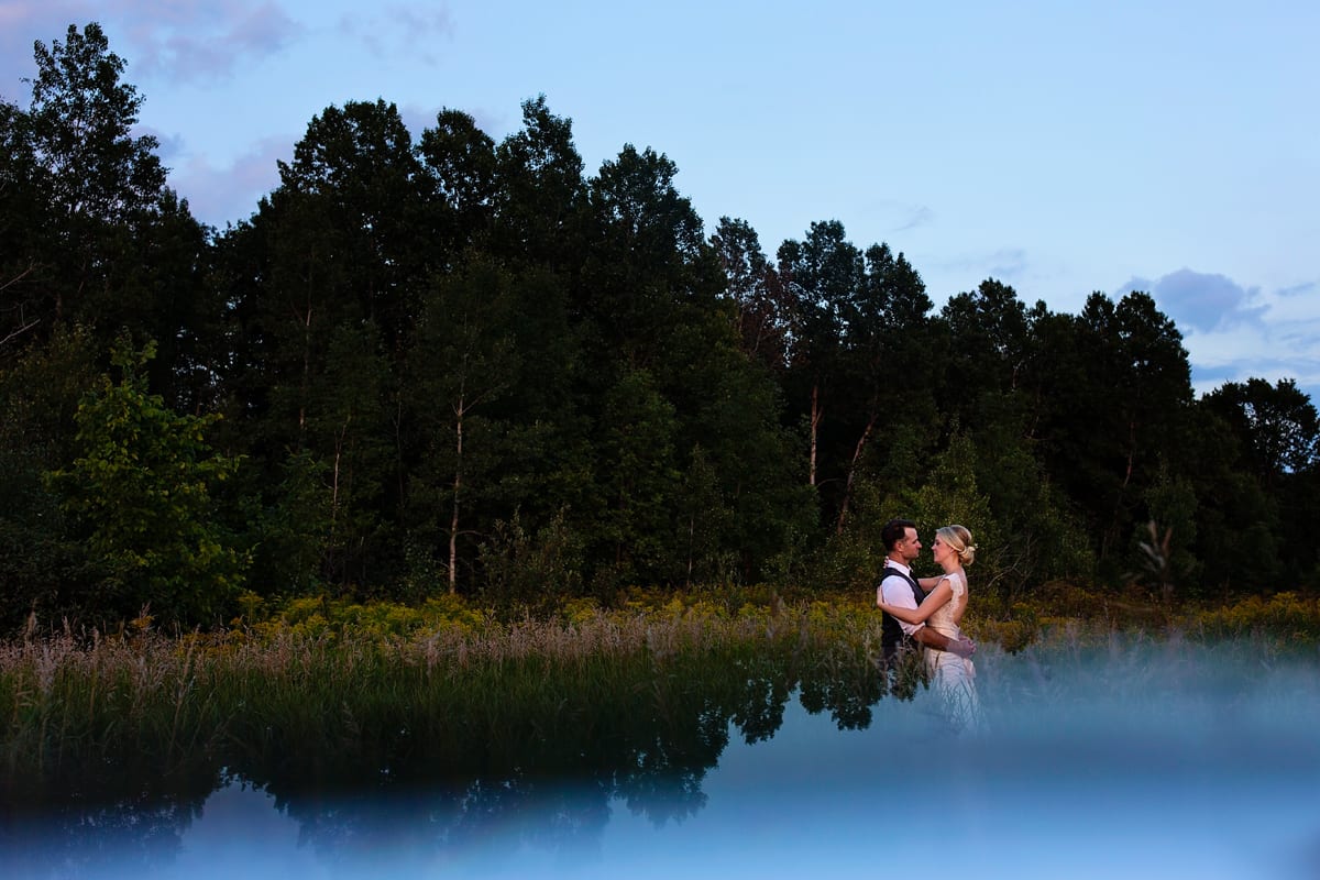 Bride and groom in evergreen tree stand with reflection