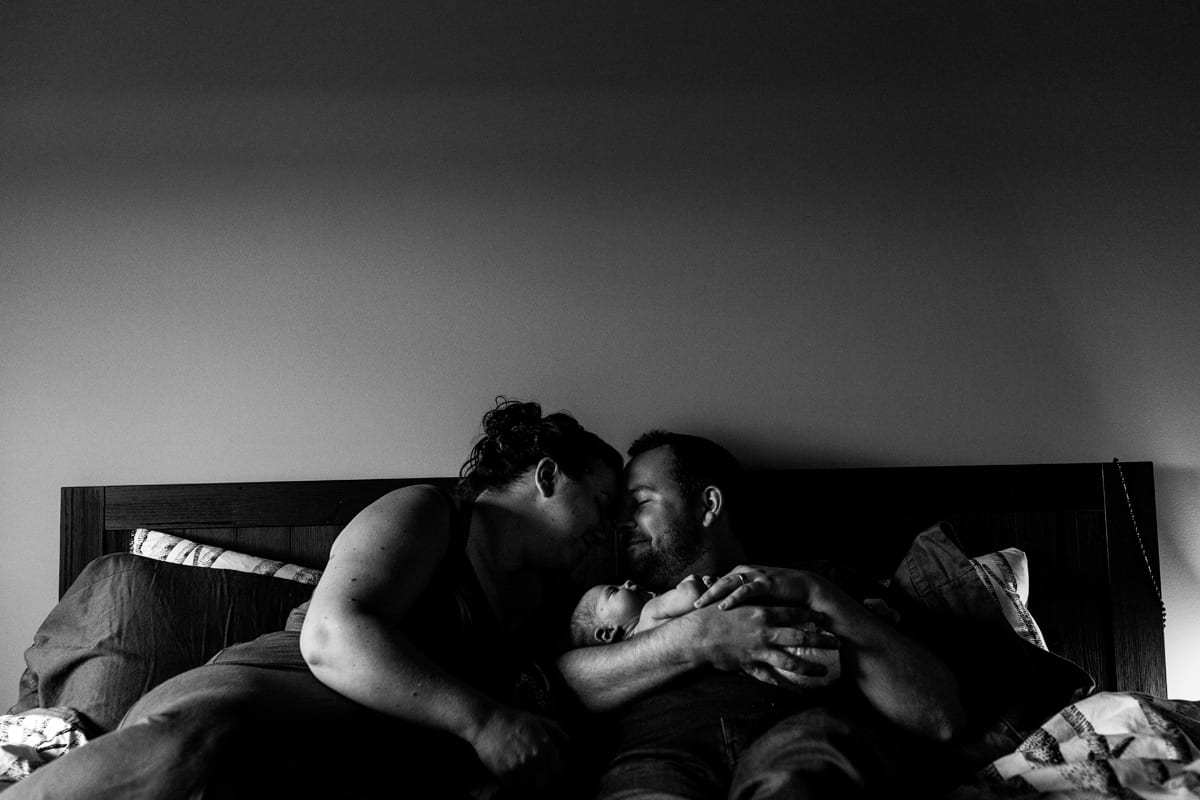 Couple eskimo kissing on bed holding newborn