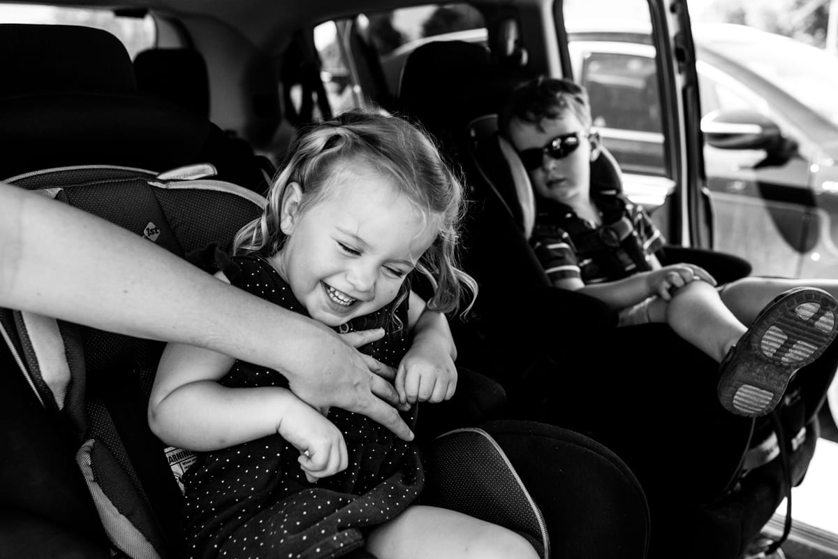 Brother and sister laughing and being tickled in backseat