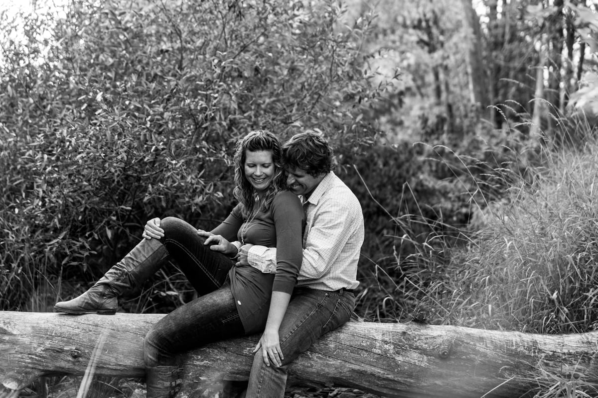 woman leaning on fiance on downed tree trunk in summer engagement session