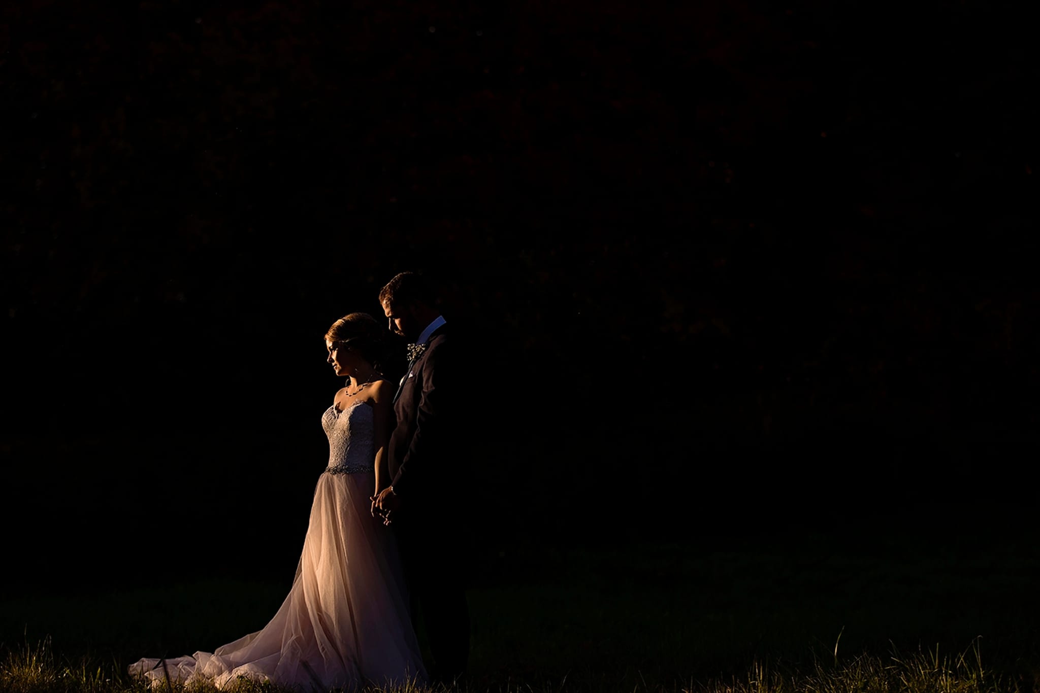 bride in blush gown faces sun with groom behind her during Autumnal NAV Centre Cornwall Wedding