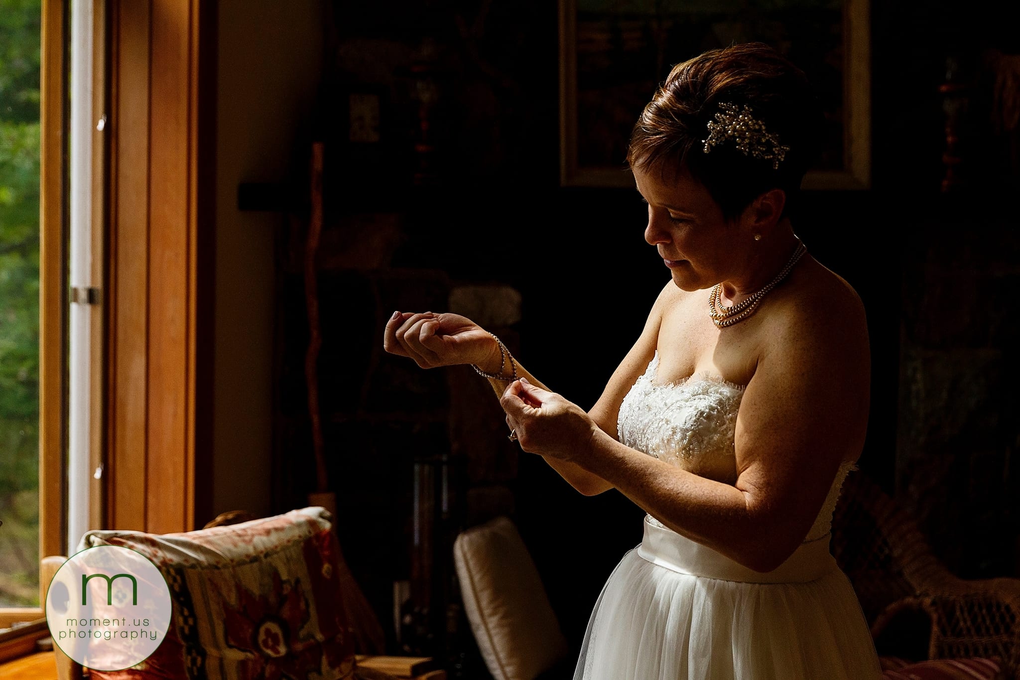 bride fastens jewellery in soft window light before Calabogie wedding