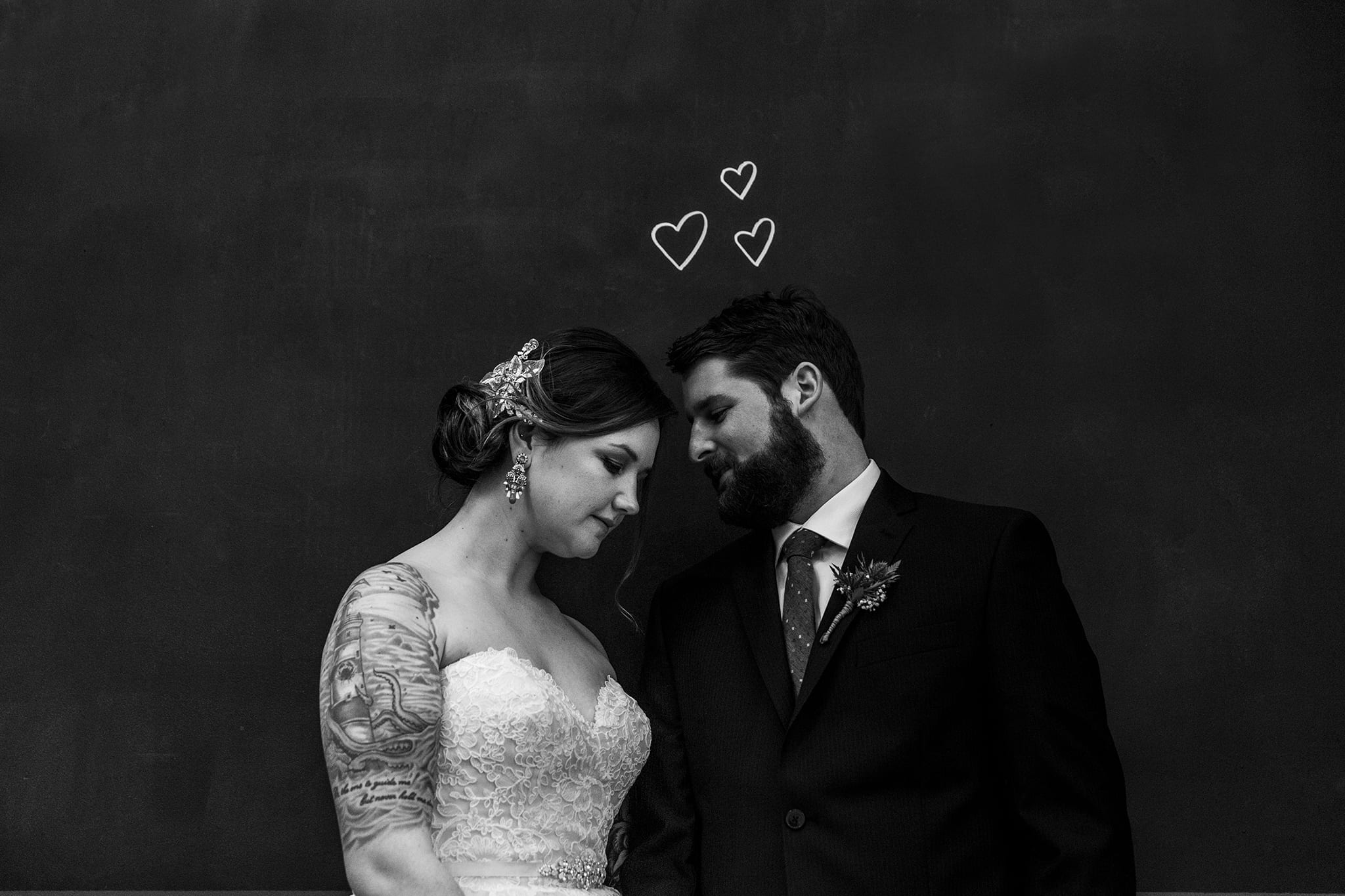 couple stand together under hearts drawn on chalkboard