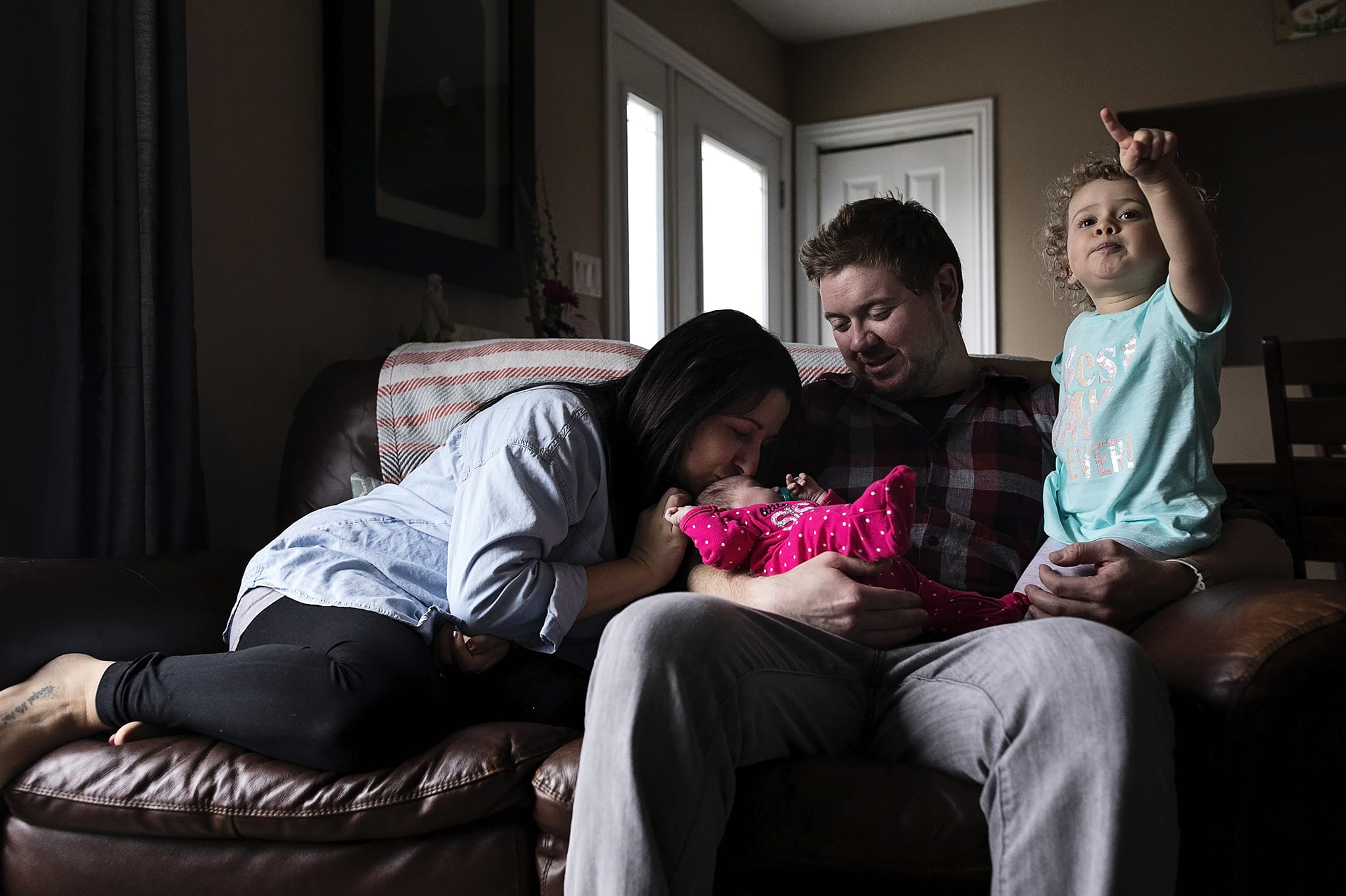 mother kisses baby while daughter points at TV