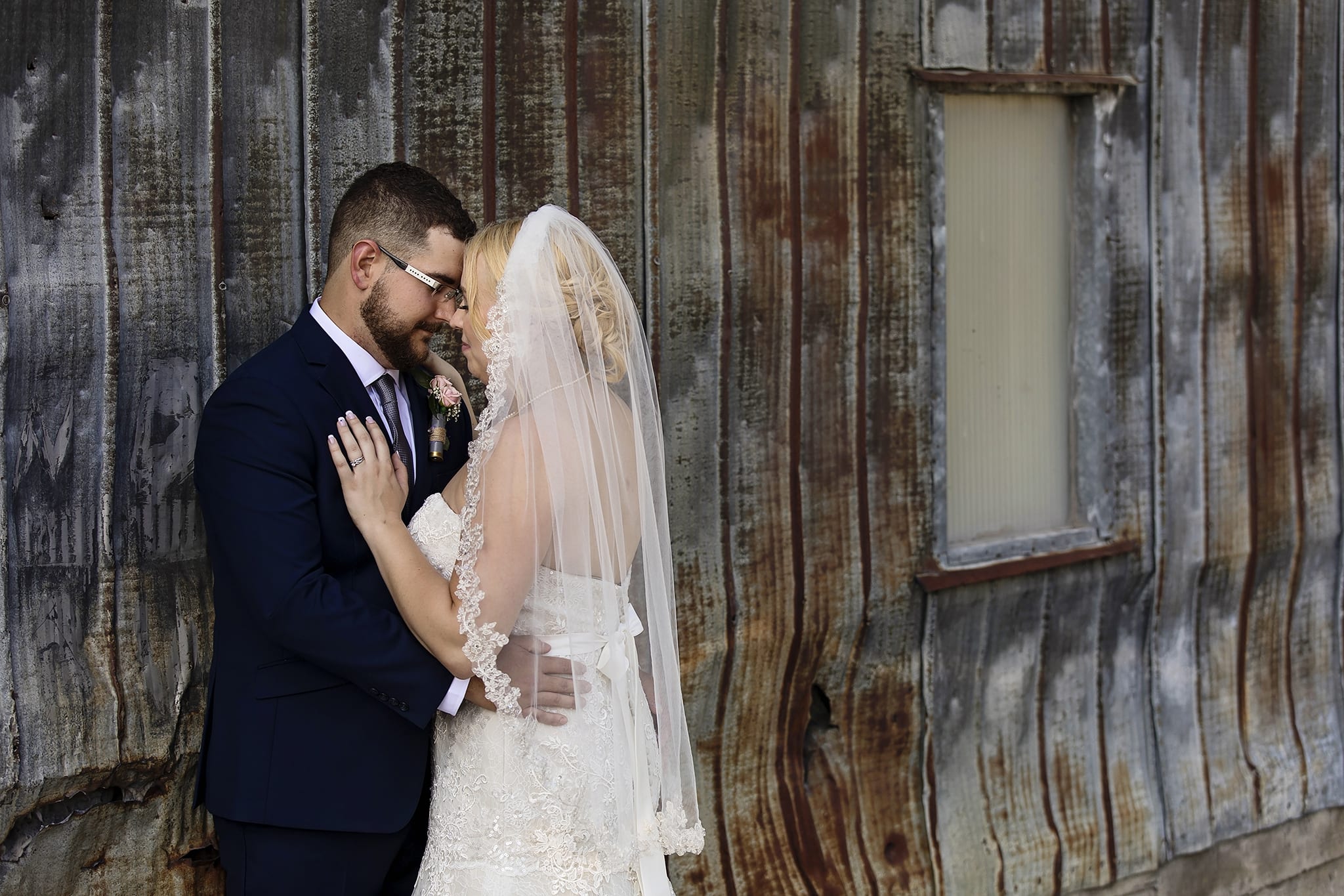 bride leans into groom's embrace in front of tin shed during summer Williamstown Fairgrounds wedding