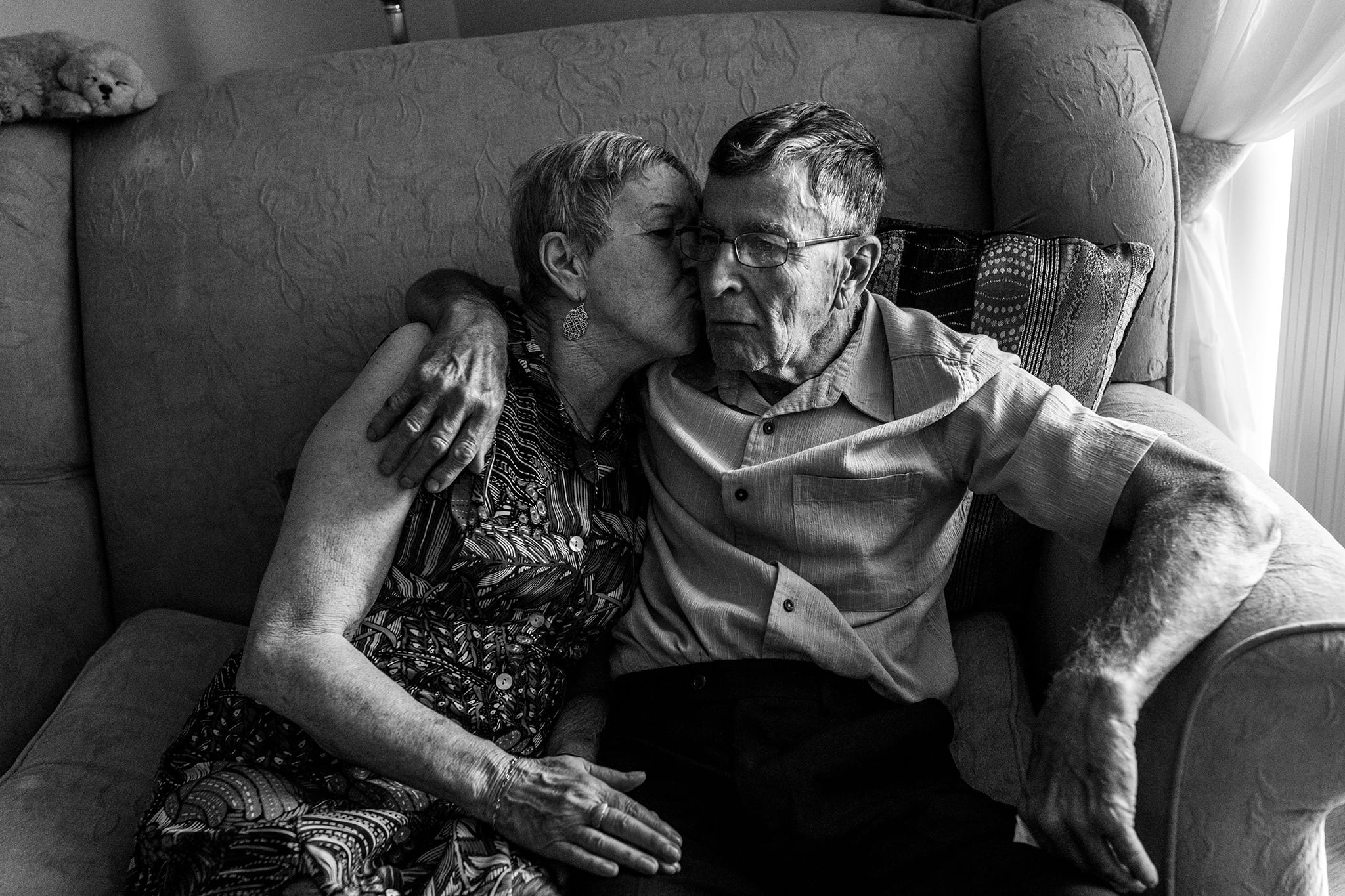 woman kisses husband's cheek while sitting on the couch