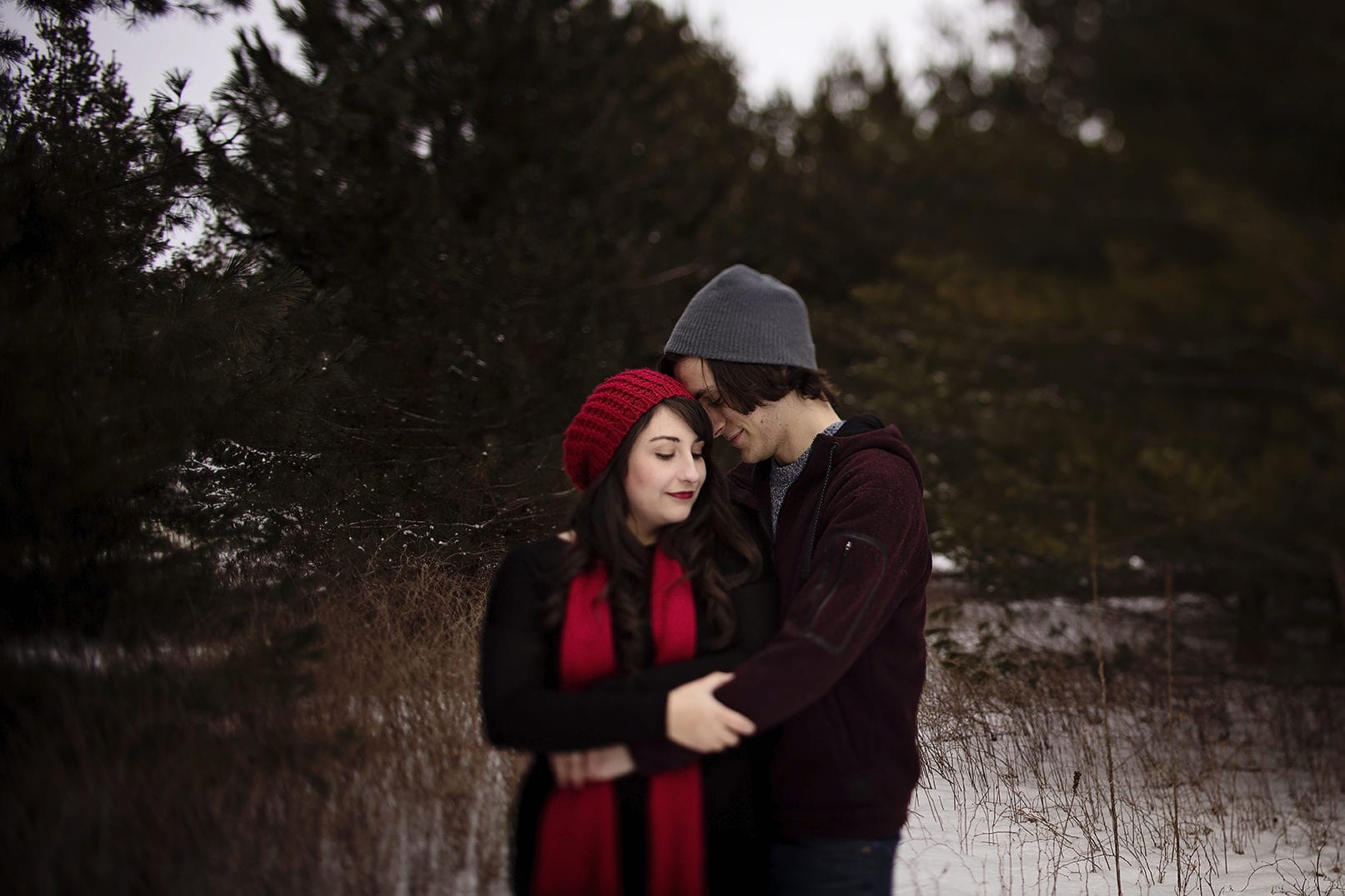 young couple wearing beanies embracing in snowy patch during winter engagement session
