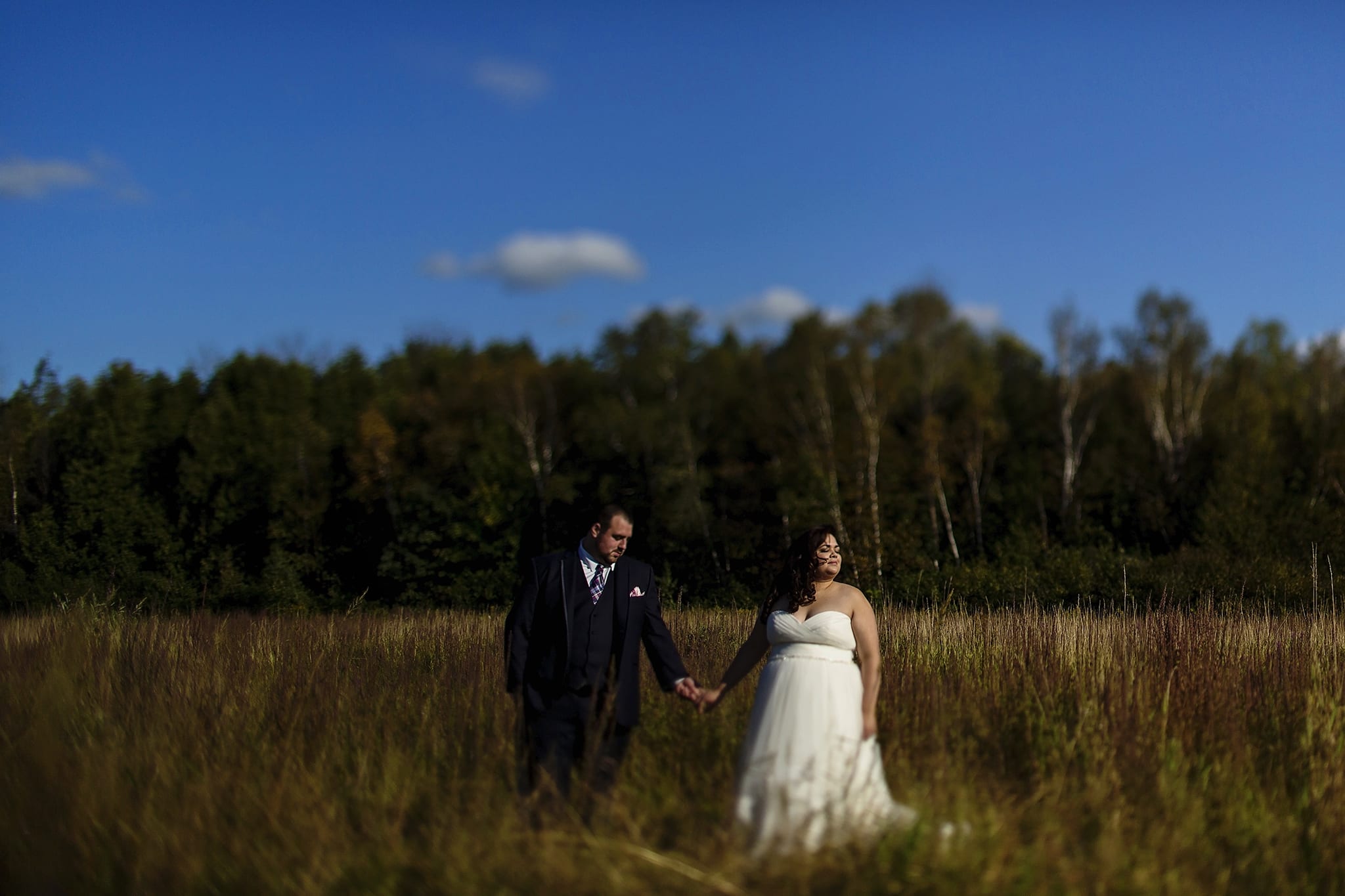 groom holds bride's hand while bride looks towards the sun