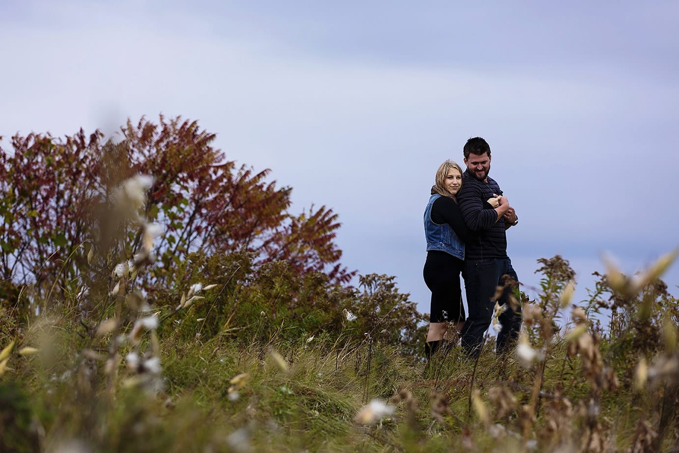 couple embracing on top of grassy hill in woodsy engagement session