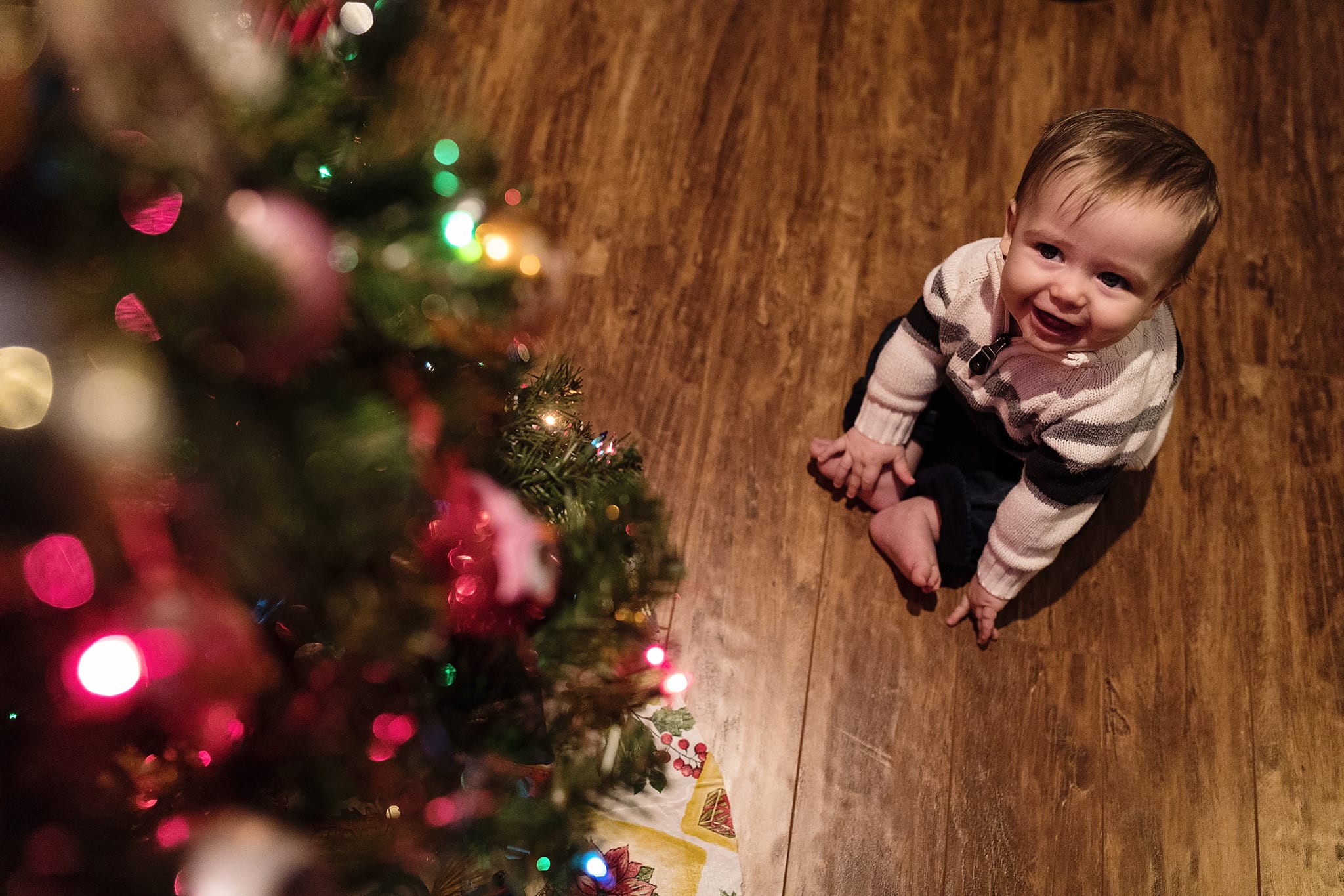 baby sits in front of Christmas tree grinning at lights