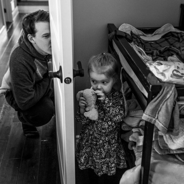 girl stands still while dad peeks through door at her