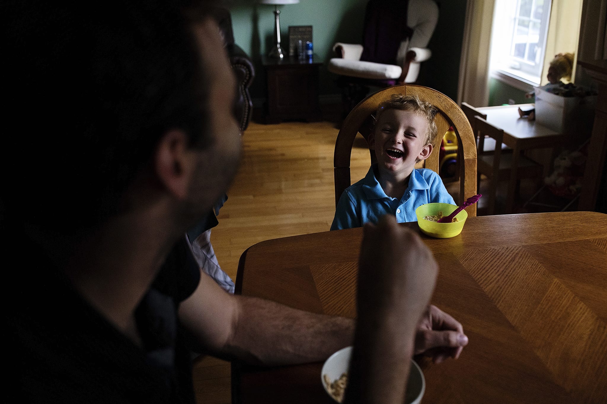 boy in blue shirt laughs at breakfast table with father