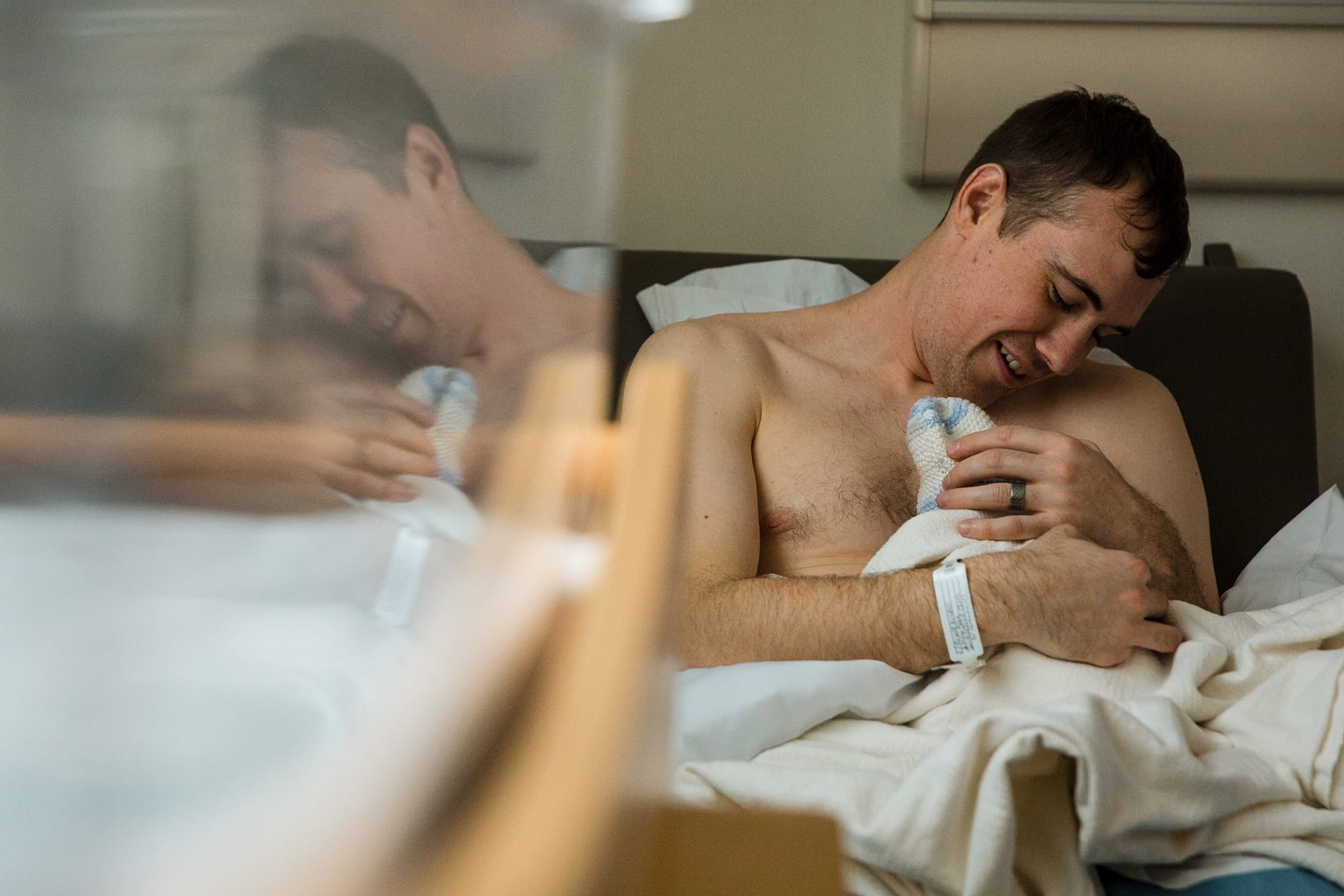 topless man holds newborn baby against chest while looking down at her