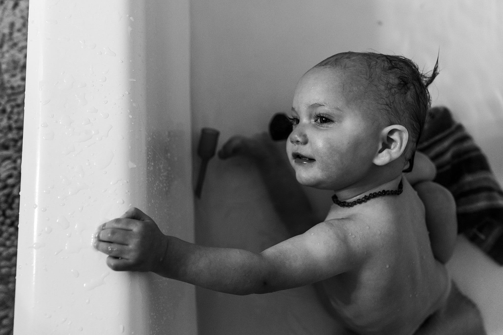 girl in bathtub holds onto edge and tilts head