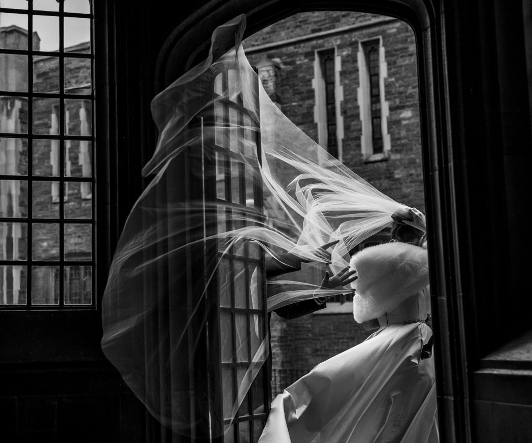 bride walks through doorway as veil gets caught in wind gust and groom catches it