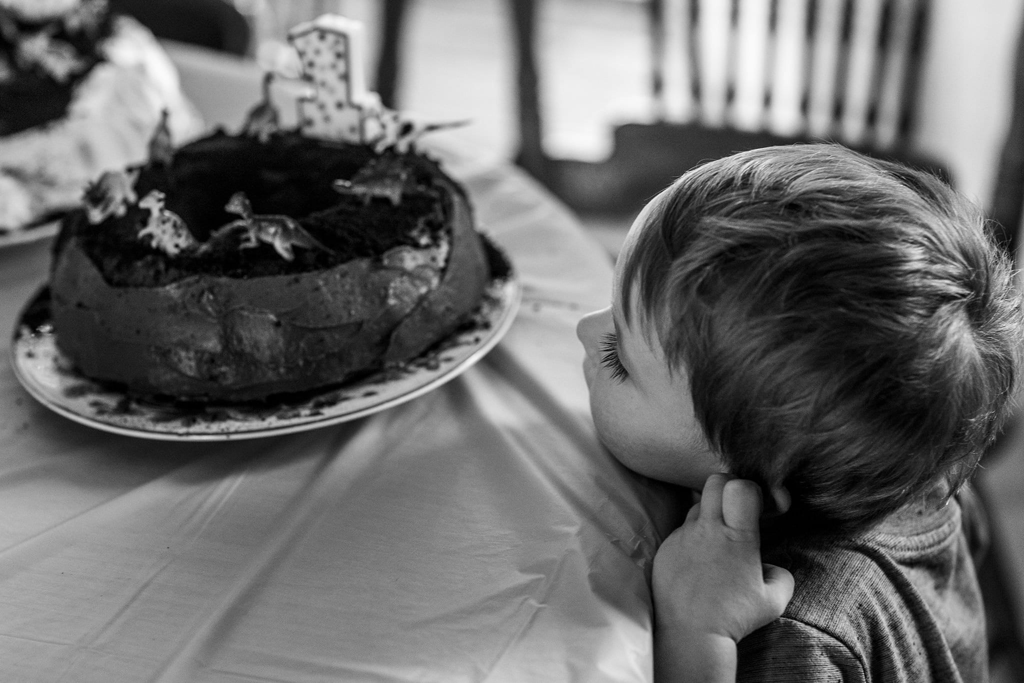 boy rests chin on table and looks intently at birthday cake