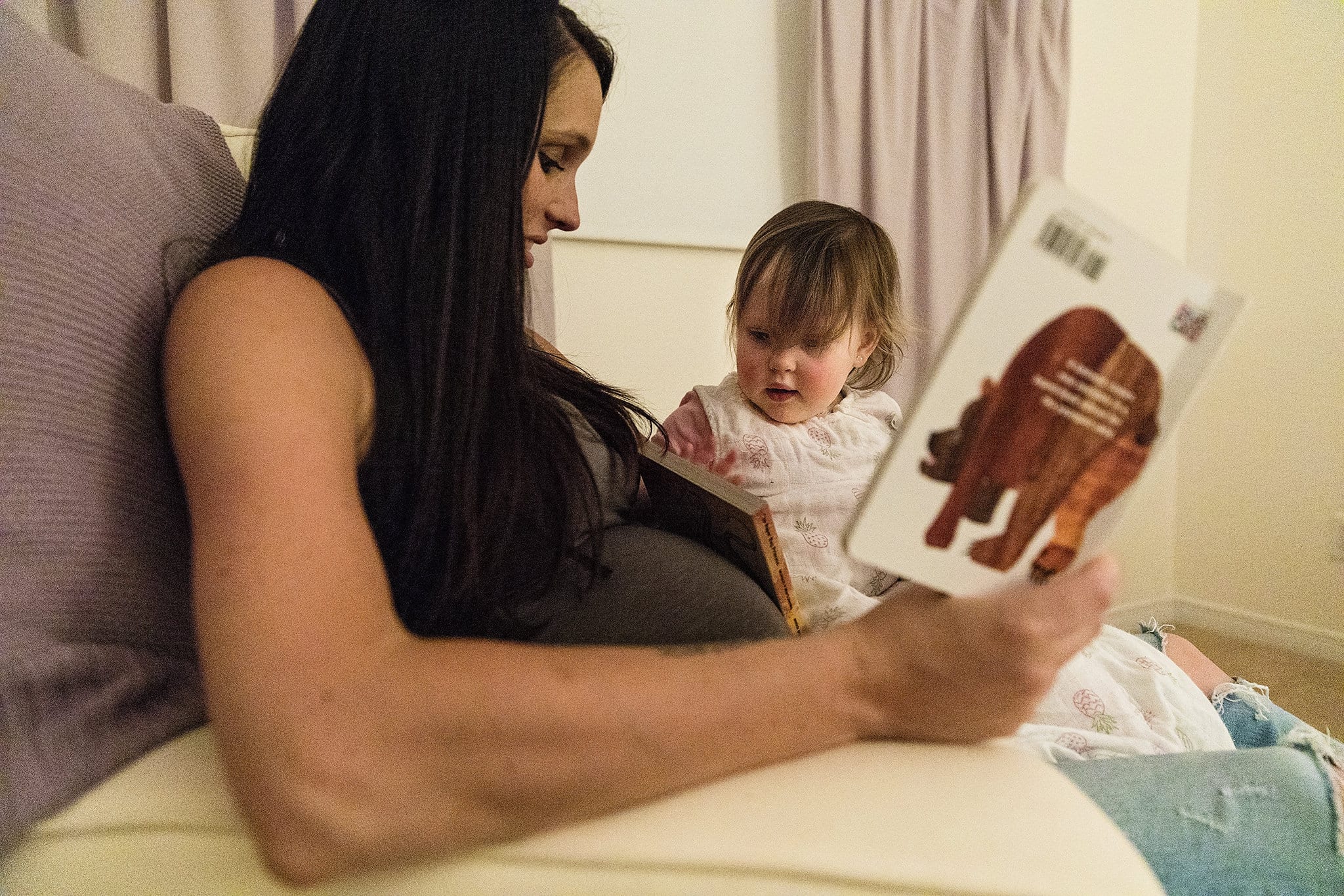 toddler leans book against pregnant Mom's belly