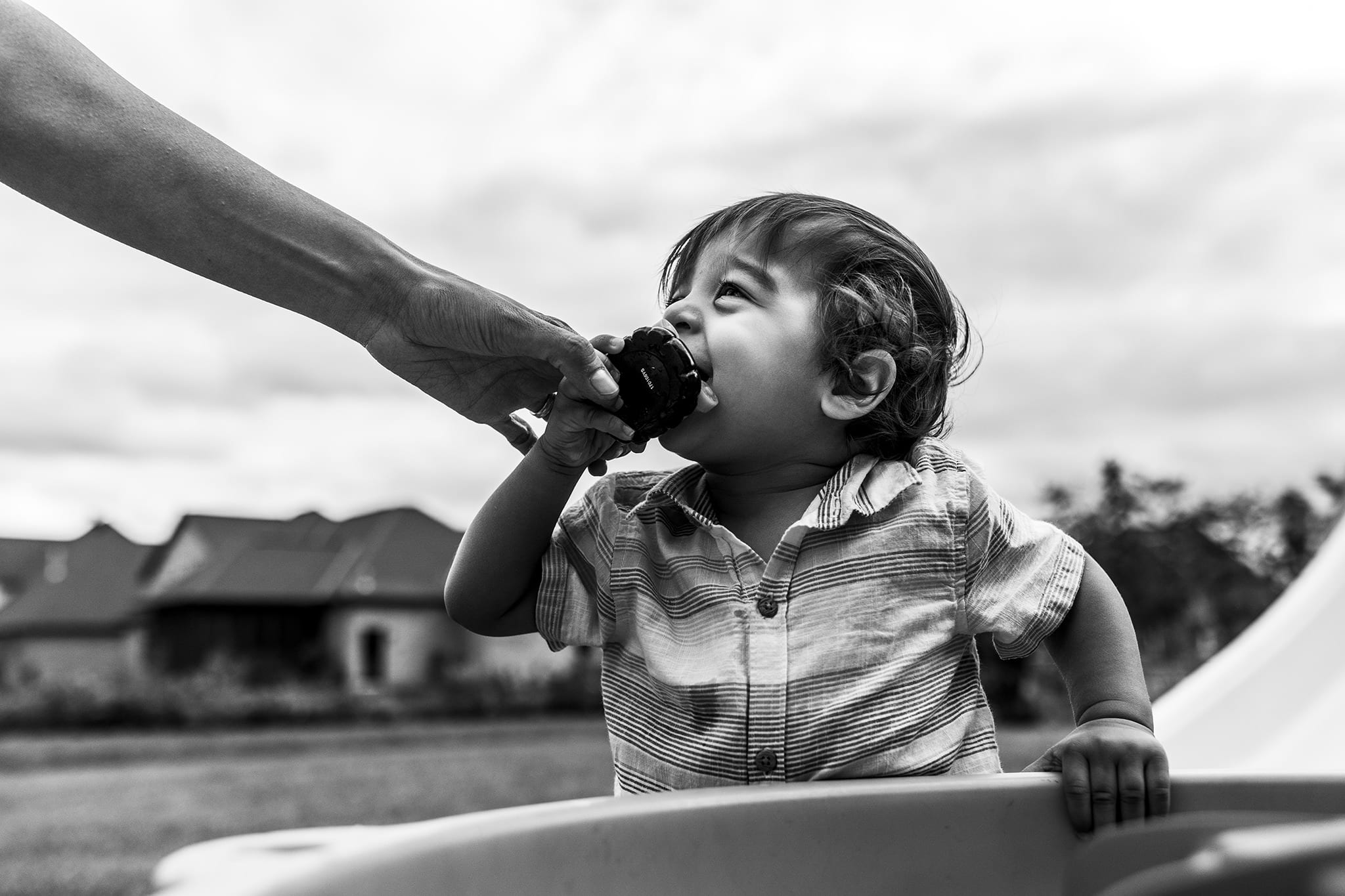 little boy puts toy in mouth while adult hand reaches to remove it