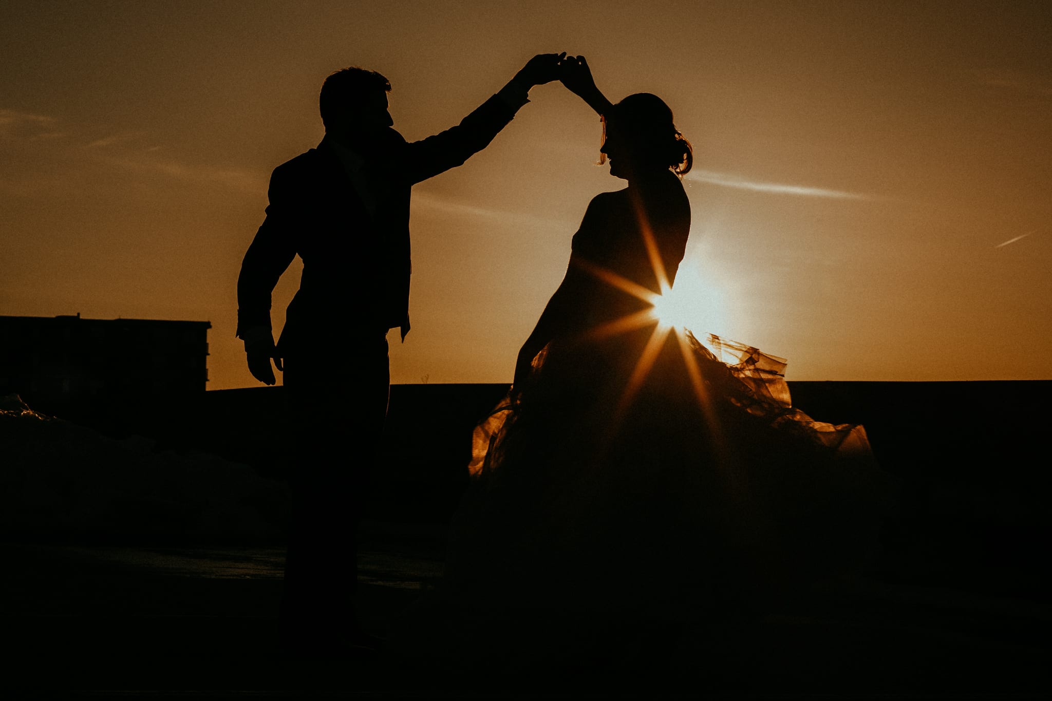 groom twirls bride as sun sparkles behind her