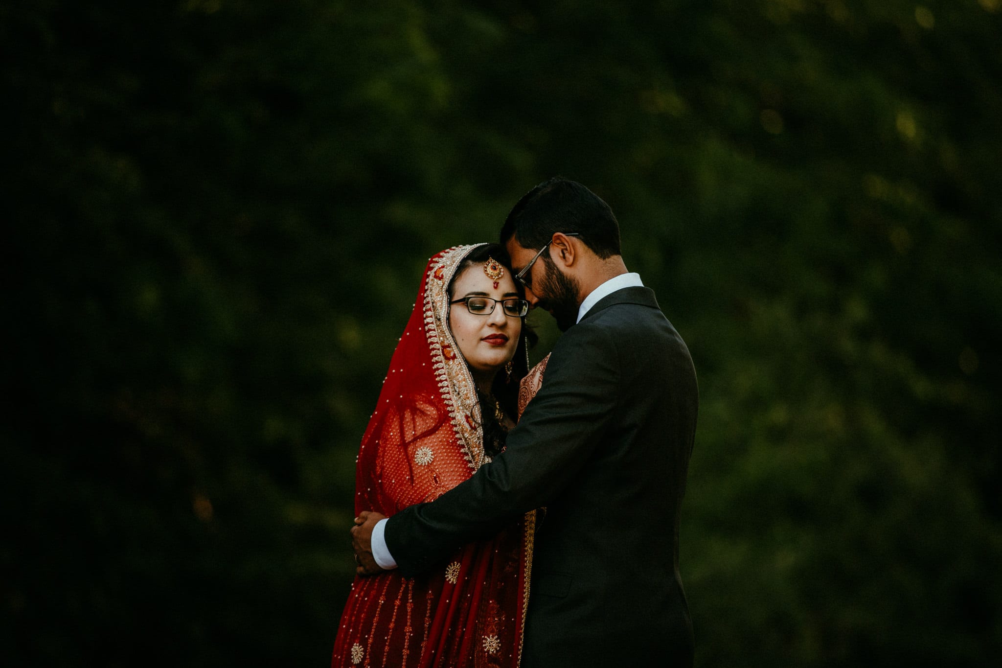 Pakistani bride in red lengha stands close to groom