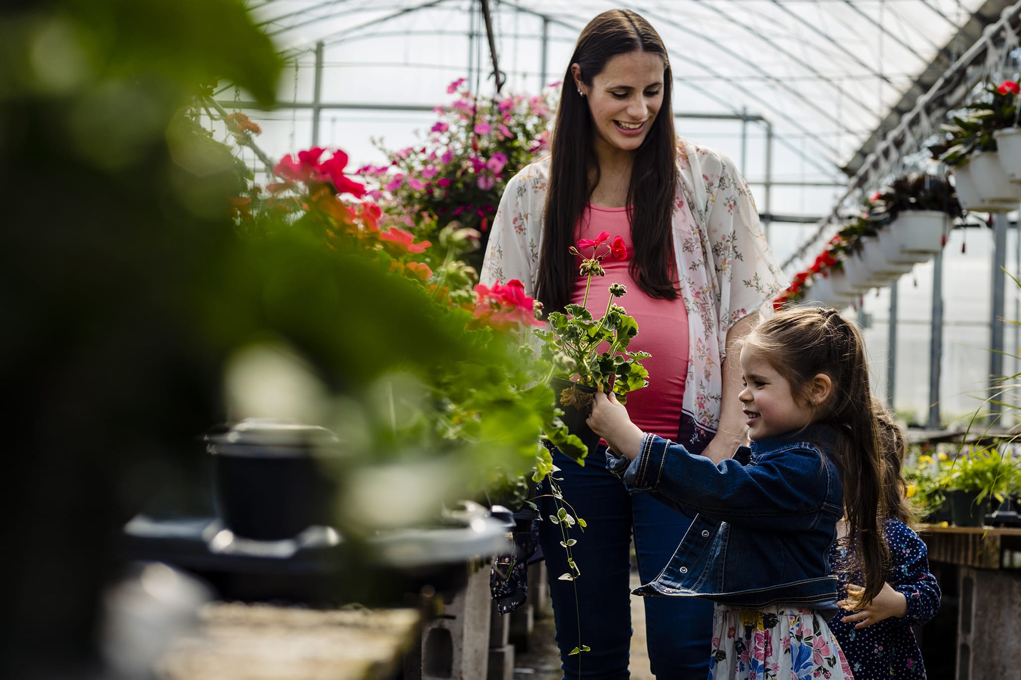 pregnant woman in greenhouse smiles at daughter choosing flowers