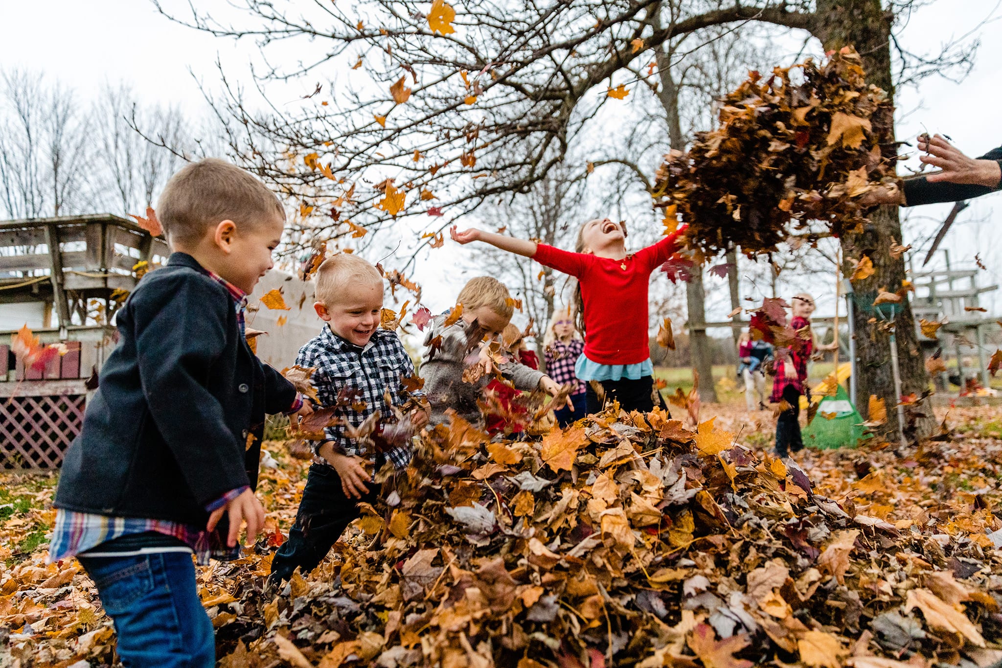 girl in red sweater throws leaves while surrounded by cousins