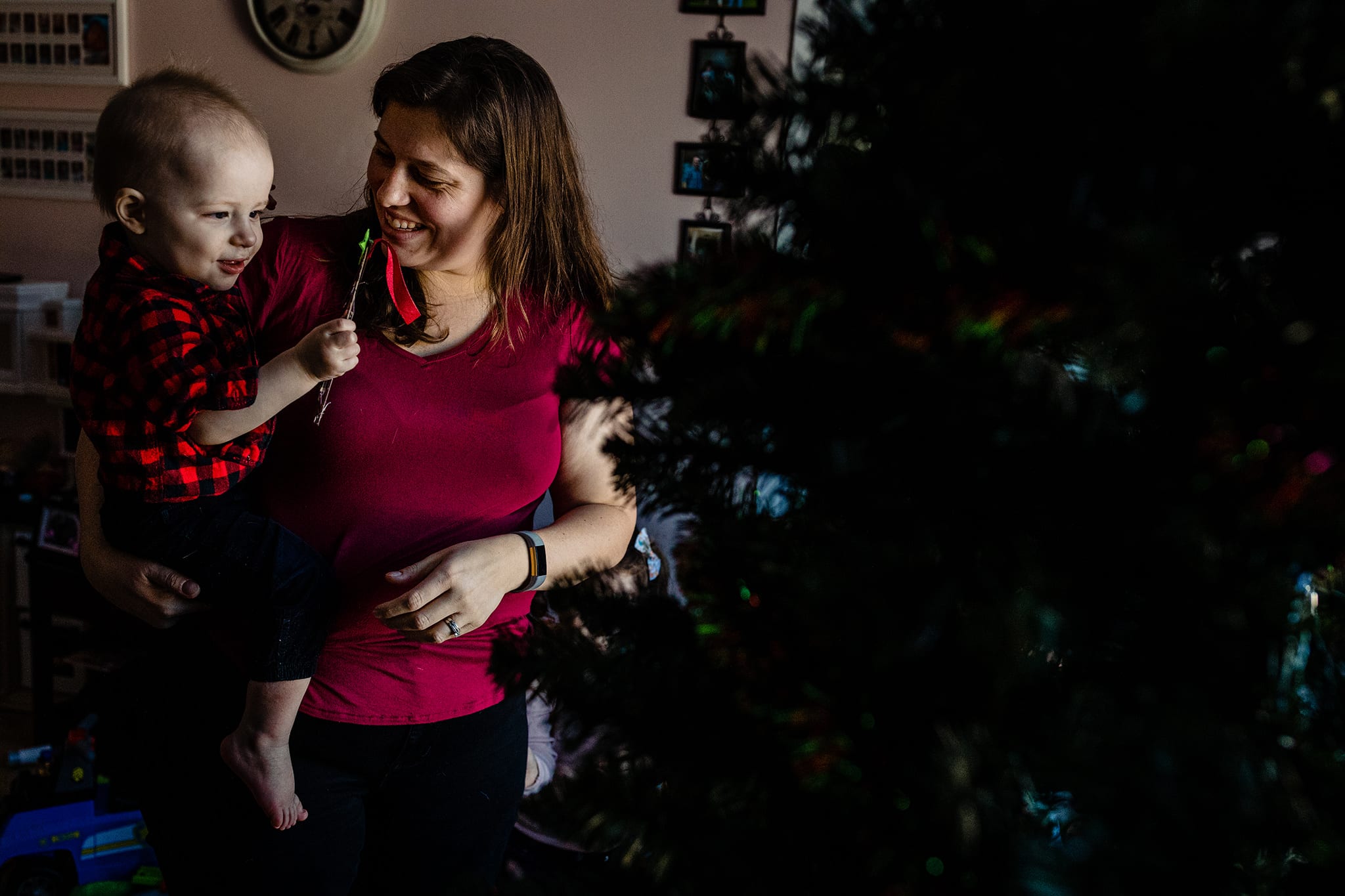 mom smiles at boy in her arms looking at Christmas ornament